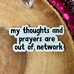 May include: White sticker with black text that reads "my thoughts and prayers are out of network" on a wooden surface.