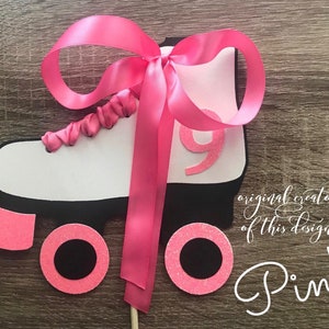May include: Pink roller skate cake topper with a pink satin ribbon bow. The skate is white with black wheels and a pink glitter accent. The number 9 is on the side of the skate.