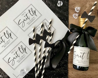 May include: Three white cards with black text that reads "Time to Suit Up. Will you be my Best Man?" and "Time to Suit Up. Will you be my Groomman?"  A small bottle of champagne with a black bow and a black and white striped straw. The straw has a black bowtie attached to it.