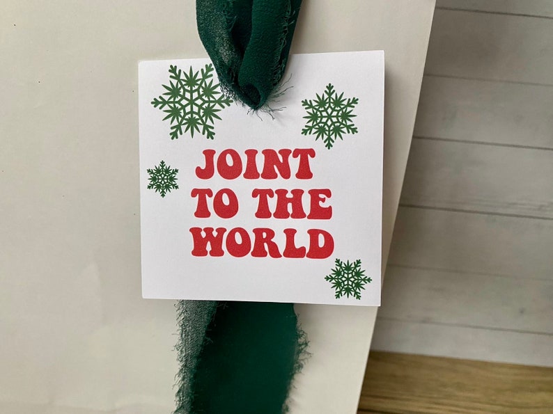 May include: White gift tag with green snowflakes and red text that reads "Join to the World". The tag is tied with a green ribbon.