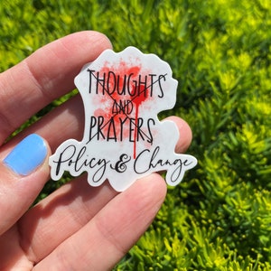 May include: White sticker with the text "Thoughts and Prayers" crossed out with a red splatter and the text "Policy & Change" below.