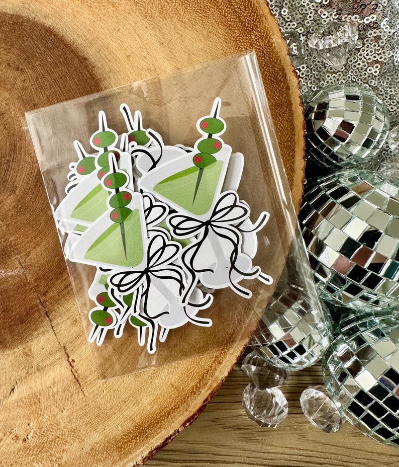Puede incluir: Una bolsa de pl&aacute;stico transparente llena de pegatinas de vaso de martini verde y rojo. Las pegatinas tienen una aceituna verde y una cereza roja en un palillo.