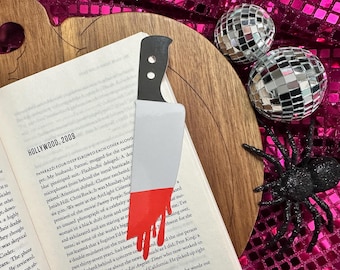 May include: A knife-shaped bookmark with a red blood drip design, placed in a book. The page shows the text "HOLLYWOOD, 2009". The image also features disco balls and a black spider, creating a Halloween theme.
