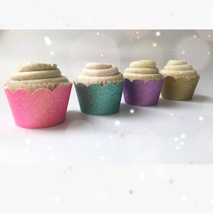 Op de afbeelding: Vier cupcakes met lichtbruine frosting en glinsterende geschulpte wrappers in roze, teal, paars en goud. De cupcakes zijn in een rij gerangschikt.