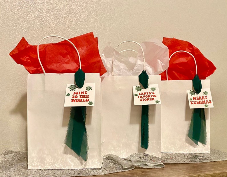 May include: Three white gift bags with green ribbon and festive tags. The tags read "Join the World", "Santa's Favorite Stoner", and "Merry Kushmas".
