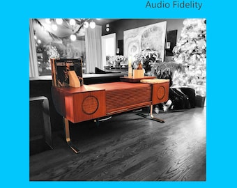 Puede incluir: Un mueble estéreo de madera de estilo moderno de mediados de siglo, con tocadiscos y altavoces. El mueble es marrón con patas doradas y cubiertas de altavoces circulares. El texto "BAUHAUS Audio Fidelity" está en la parte superior y "Fusion of Art, Design and Engineering" en la inferior.