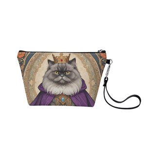May include: A gray and white cat wearing a gold crown and purple robe, with a gold and blue jeweled collar, is featured on a cosmetic bag with a black zipper and a black strap.