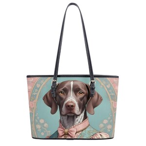 May include: A brown and white dog with a pink bow tie is featured on a light blue tote bag with a floral pattern. The bag has black leather straps and a zipper closure.