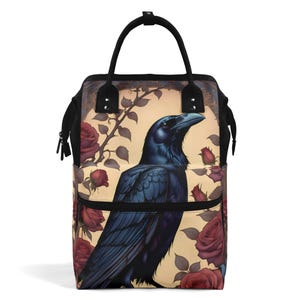 May include: A black backpack with a large raven and roses printed on the front. The raven is perched on a branch with roses in bloom. The backpack has a black zipper and a black handle.