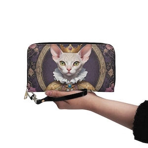 May include: A black leather wallet with a gold zipper and a colourful print of a cat wearing a crown and a royal robe. The wallet has a black strap.
