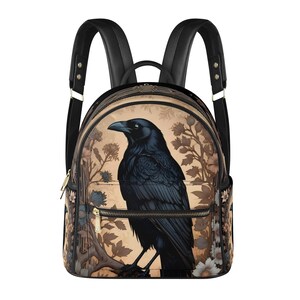 Puede incluir: Una mochila de cuero negro con correas ajustables. La parte delantera de la mochila presenta una ilustración detallada de un cuervo negro posado en una rama con detalles florales en tonos marrones, crema y dorado.