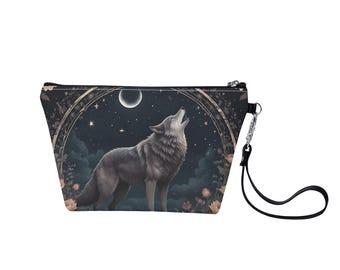 Puede incluir: Una bolsa de maquillaje negra con cremallera con un lobo aullando a la luna. El lobo es gris y blanco y está rodeado de estrellas y flores. La bolsa tiene una correa negra.