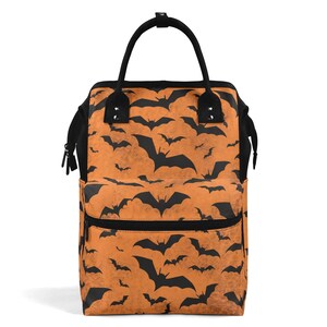 May include: A black and orange nappy bag with a bat pattern. The bag has two zipped pockets on the front and a top handle.