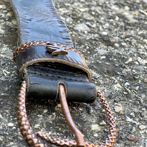 Pode incluir: Um cinto de couro castanho com uma fivela de cobra de cobre. A fivela é detalhada com um padrão de pele de cobra.