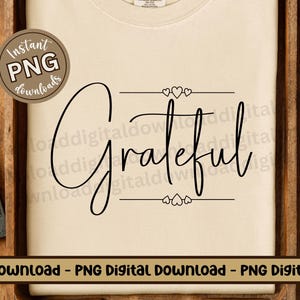 May include: A white t-shirt with the word "Grateful" written in black cursive script. The word is framed by two horizontal lines with three small hearts above and below the word.