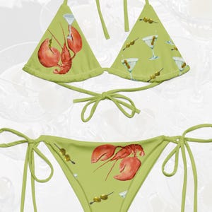 Peut inclure: Un bikini vert imprimé de homards et de martinis. Le haut est de style triangle et le bas est de style échancré.