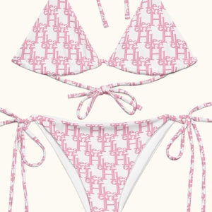 Puede incluir: Conjunto de bikini blanco con un patrón rosa repetido de la palabra "Heart" y la letra "H". La parte superior es de estilo triángulo con correas anudadas, y la parte inferior es de corte clásico con laterales anudados.