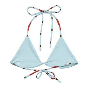 May include: A light blue bikini top with a triangle shape. The straps are light blue with brown polka dots and red accents. The top ties at the neck and back. The bikini top is a swimwear item.