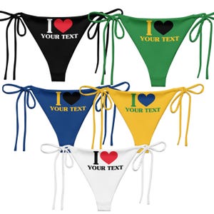 May include: A collection of five bikini bottoms in various colors: black, green, blue, yellow, and white. Each features a tie-side design and the text "I YOUR TEXT" with a heart symbol. The heart color varies.