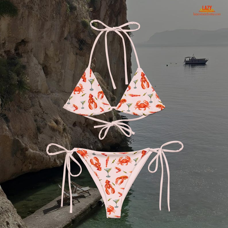K&ouml;nnte beinhalten: Zweiteiliger Bikini mit wei&szlig;em Hintergrund und einem sich wiederholenden Muster aus roten Hummern, Krabben und Martinigl&auml;sern. Das Oberteil ist im Triangel-Stil gehalten, die Hose hat Bindeb&auml;nder.