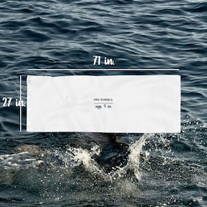 May include: A white beach towel, 71 inches long and 27 inches wide, floats on water. The towel has the text "MRS. ROBERTS" and "app. 9 in." printed on it. The water is dark blue with white splashes.