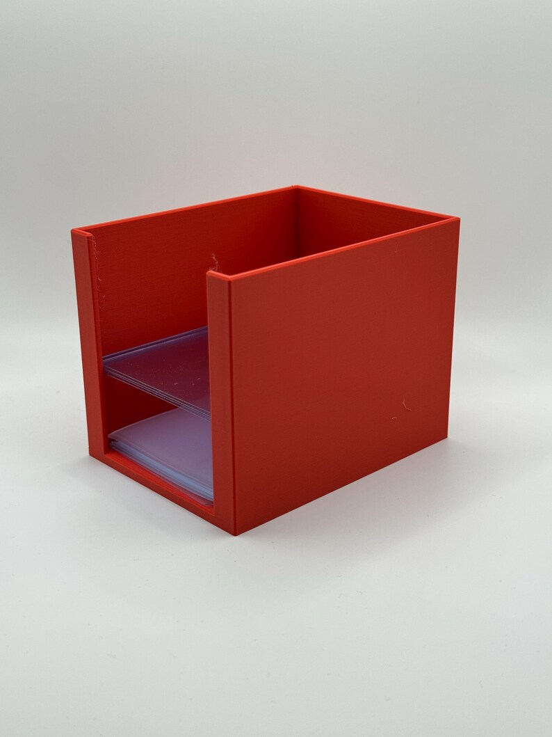 May include: A bright red, rectangular desk organizer with two clear plastic shelves. The organizer is made of solid material and has a simple, modern design. The shelves are designed to hold small items.
