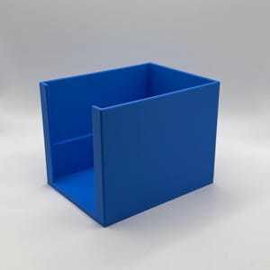 May include: A vibrant blue, open-top box, likely for storage or organization. The box has a rectangular shape with a solid base and sides. The color is a bright, solid blue, and the box appears to be made of a smooth material.