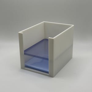 May include: A white, rectangular desk organizer with a blue, transparent shelf. The organizer has an open top and a slot for storing items. The design is minimalist and modern, suitable for office or home use.