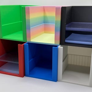 May include: A collection of colorful, open-faced storage cubes. The cubes are in various colors, including green, red, blue, black, and white. One cube features a rainbow gradient. Each cube has a rectangular shape and is designed for organizing small items.