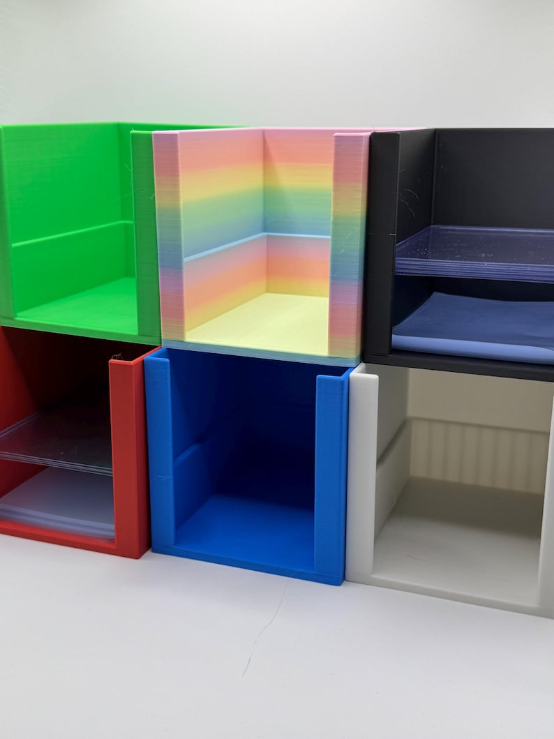May include: A collection of colorful, open-faced storage cubes. The cubes are in various colors, including green, red, blue, black, and white. One cube features a rainbow gradient. Each cube has a rectangular shape and is designed for organizing small items.