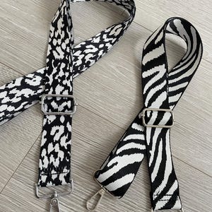 May include: Two black and white patterned adjustable straps with silver hardware. The straps are made of fabric and have a leopard print and a zebra print.
