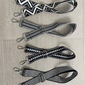 May include: Four black and white patterned straps with silver metal clasps. The straps are made of woven fabric and have different geometric patterns.