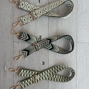 May include: Three patterned bag straps with gold-tone hardware. The straps feature geometric designs in various colour combinations: white and black, black and green, and green and white. Each strap has a metal buckle and two clasps.