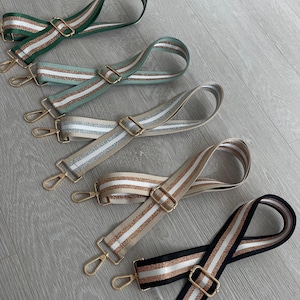 May include: Five different coloured fabric straps with gold hardware and a white glitter stripe. The straps are arranged in a row from top to bottom, with the green strap at the top and the black strap at the bottom.