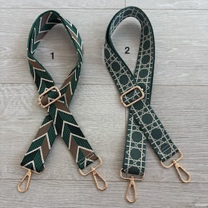 May include: Two decorative bag straps with gold-coloured hardware. One strap features a green, brown, and white chevron pattern. The other strap has a green geometric design with white accents. Both straps are shown on a light wood surface.