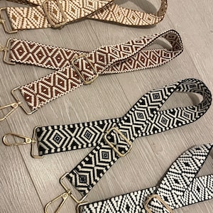 May include: Four woven fabric straps with geometric patterns in black and white, brown and white, and beige and white. The straps have gold metal clasps and swivel hooks.