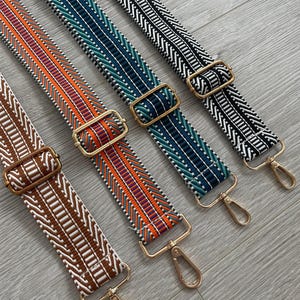 May include: Five colourful patterned fabric straps with gold metal clasps. The straps are woven with geometric designs in brown, orange, teal, and black.