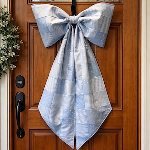 May include: A decorative bow in shades of light blue and white, patterned with squares and dots, hangs on a wooden door. The bow is made of fabric. The door has a glass window and black door furniture.