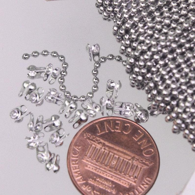 May include: A silver-toned ball chain and several matching metal connectors are displayed next to a copper-colored United States one-cent coin for scale. The chain consists of small, uniform spherical beads linked together in a continuous strand.