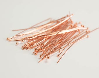 May include: A collection of rose gold head pins, each featuring a thin, straight metal shaft topped with a small, spherical ball. These jewelry-making components are arranged in a loose, overlapping pile, showcasing their metallic finish.