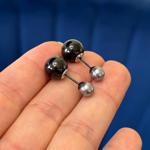 May include: A pair of black and silver double-sided earrings. Each earring features a black sphere on one side and a silver sphere on the other.