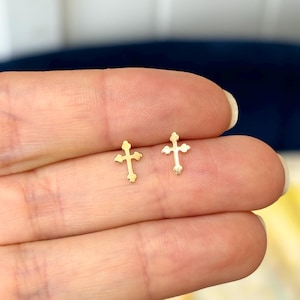 May include: A pair of gold cross stud earrings. The earrings are small and delicate, and they are perfect for everyday wear.