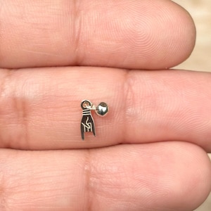 May include: A small, silver earring featuring a charm shaped like a hand making the 'rock on' gesture, with a small ball stud. The earring is designed with a polished finish, reflecting light. The earring is a piece of jewelry.