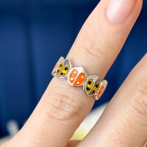 May include: A silver ring featuring a band of orange and yellow ladybirds. The ladybirds have black spots and are set in a silver band.