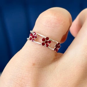 May include: A silver ring featuring three red flower-shaped accents. Each flower is made of small red rhinestones.
