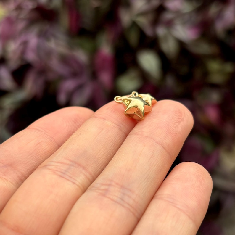 May include: Two gold star charms connected together. The charms are small and have a three-dimensional shape.