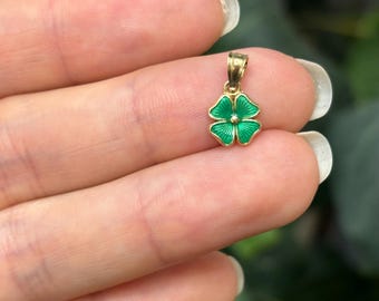 May include: A small gold pendant shaped like a four-leaf clover with green enamel.