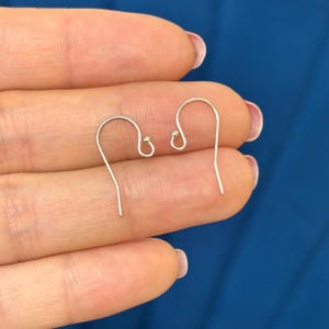 May include: Two silver-colored earring hooks with a curved design. Each hook has a small, round bead attached. The hooks are displayed against a blue background.