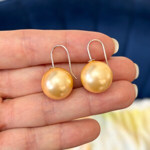 May include: A pair of gold-colored pearl drop earrings with silver hooks.