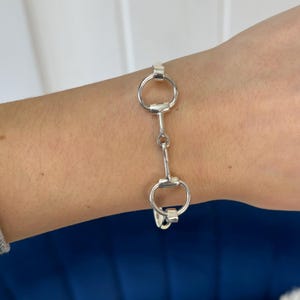 May include: A silver bracelet with a double-loop design, resembling a horse bit.